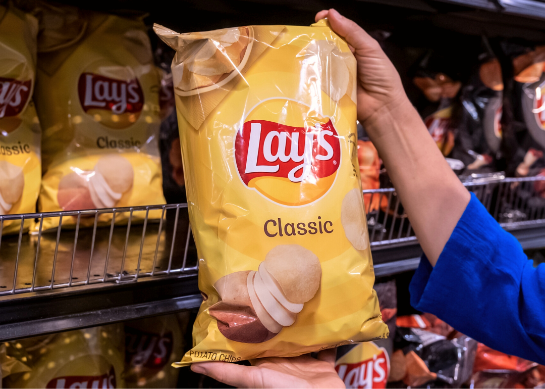 Hand holding a bag of Lay’s Chips in supermarket.
