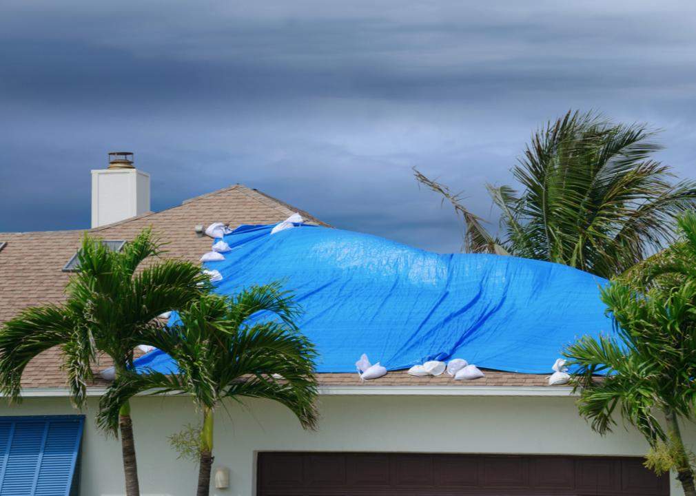 Photo shows a close-up of a house with a blue tarp attached to the roof
