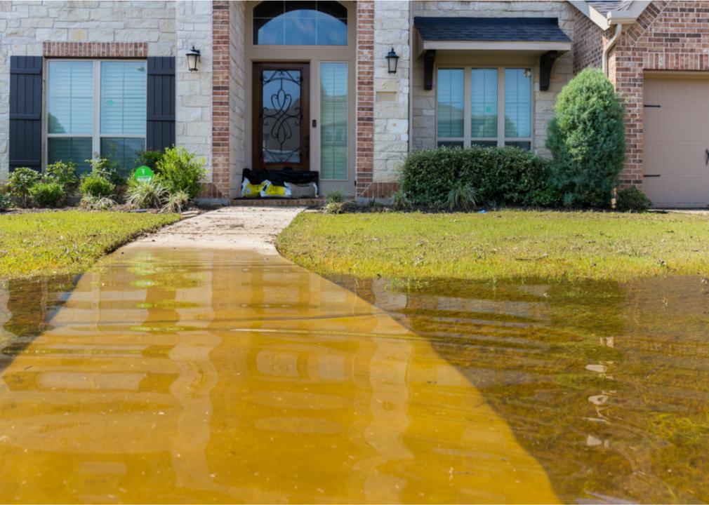 Photo shows a medium-shot of a home with flood waters approaching but not breaching the front door