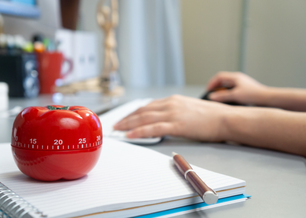 Kitchen timer in the shape of a tomato on notebook with person working on laptop in background.