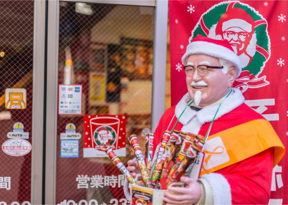 A man dressed like a Christmassy looking Colonel Sanders standing outside of a KFC.