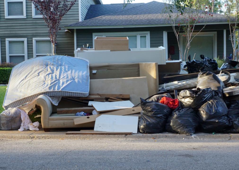 Photo shows large piles of discarded furniture and trash bags at the curb of a house 