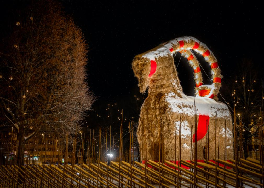 A huge straw goat outside at night, covered in a light dusting of snow.