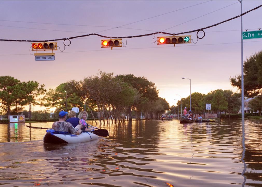 Photo shows several people sitting in a kayak in a flooded neighborhood street