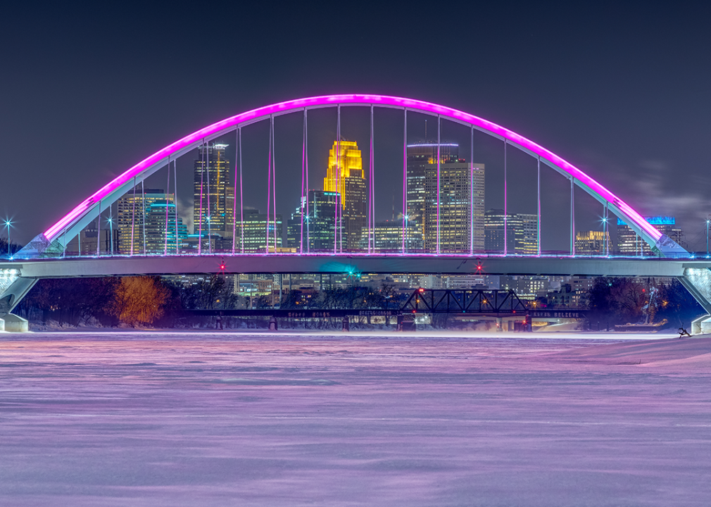 A frozen, snowy Mississippi River and magenta colored Lowry Bridge with Minneapolis skyline.