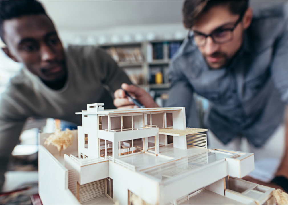 Two men work on an architectural model of a house.