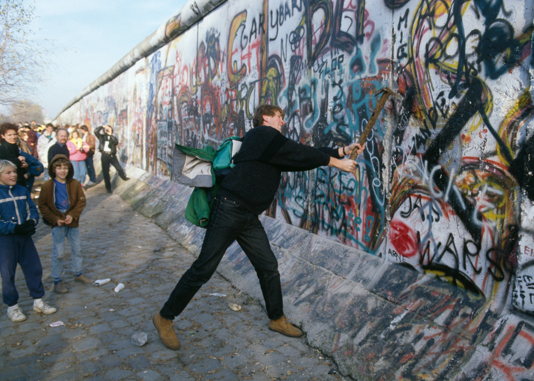 A man wields a pickaxe to the Berlin Wall.