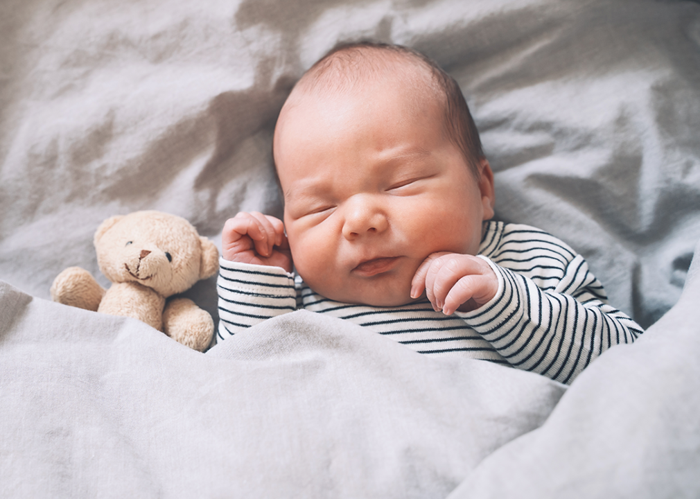 Infant sleeping beside small teddy bear.