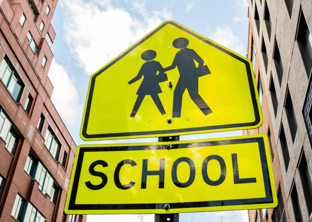 Yellow school sign with buildings in background.