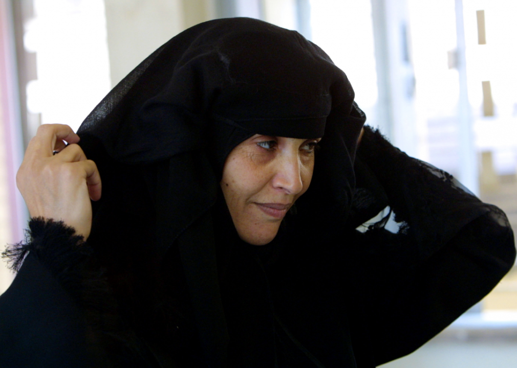 A Jordanian woman lifts her burqa to be identified before voting at a polling station