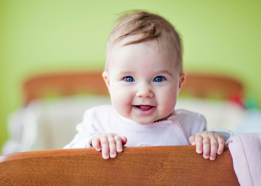 Baby standing in crib smiling.