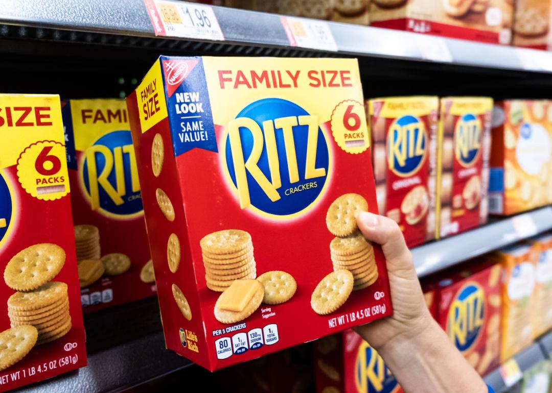 Hand holding a box of Ritz crackers in a supermarket.