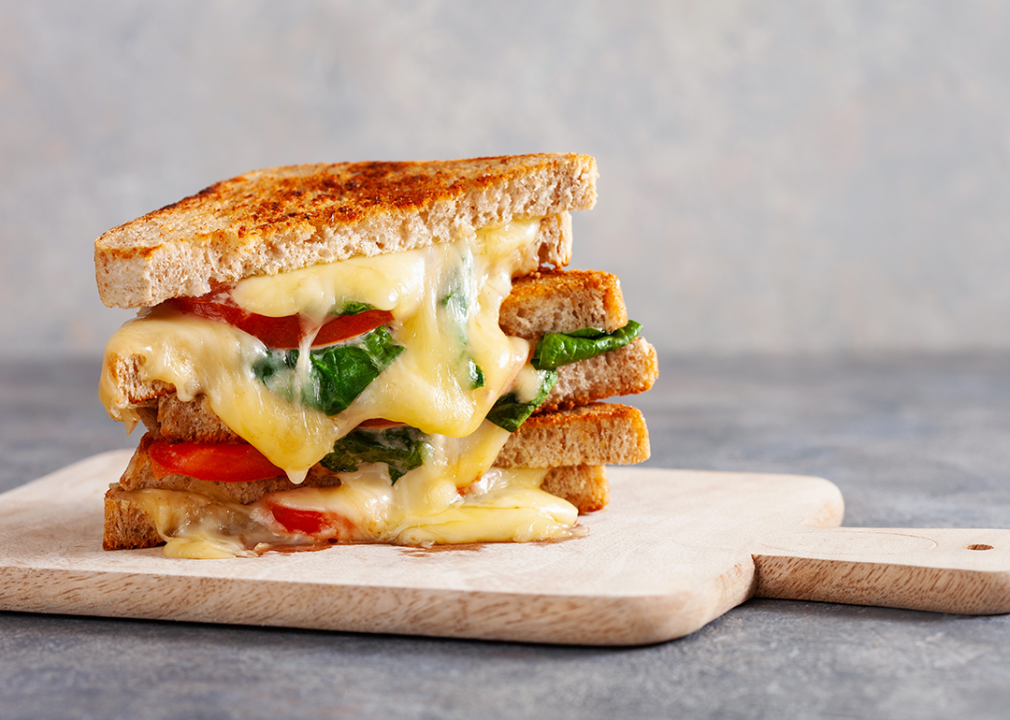 Grilled cheese sandwich with tomato and spinach on a cutting board.