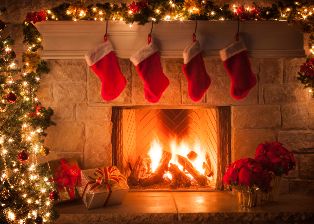 Christmas stockings and lights hang above a cozy lit fireplace.
