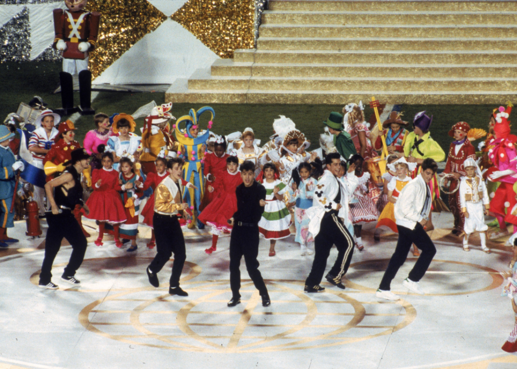 New Kids On The Block performing at a superbowl, surrounded by people in costumes.