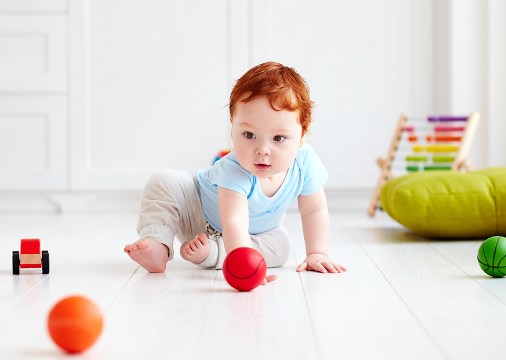 Baby crawling on floor playing with balls.