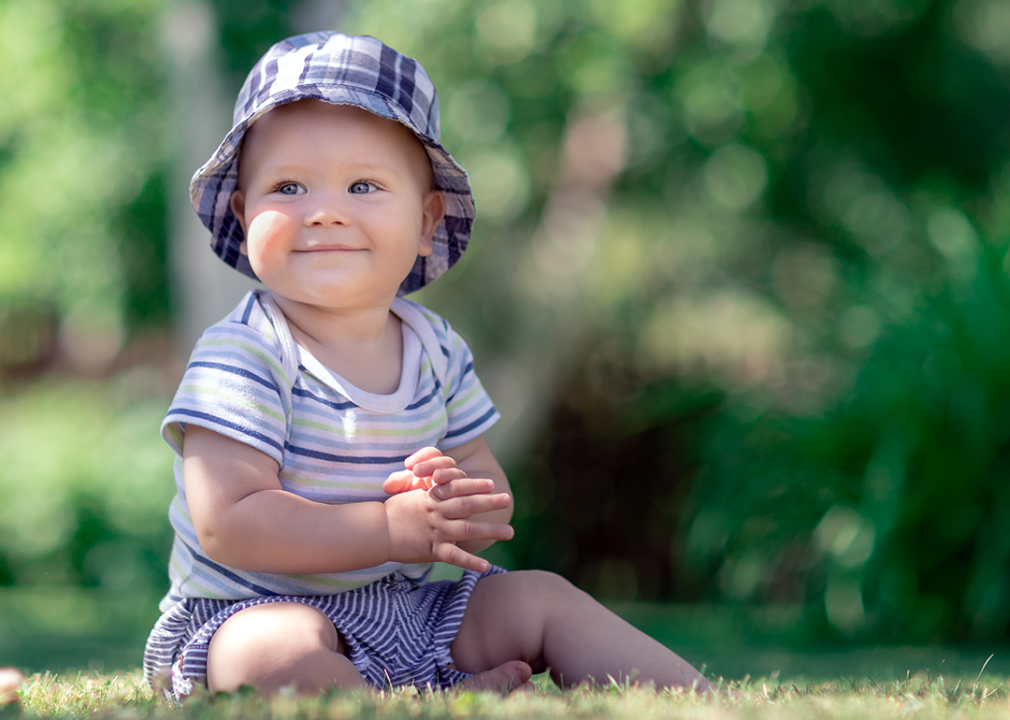 Baby wearing hat sitting in grass.