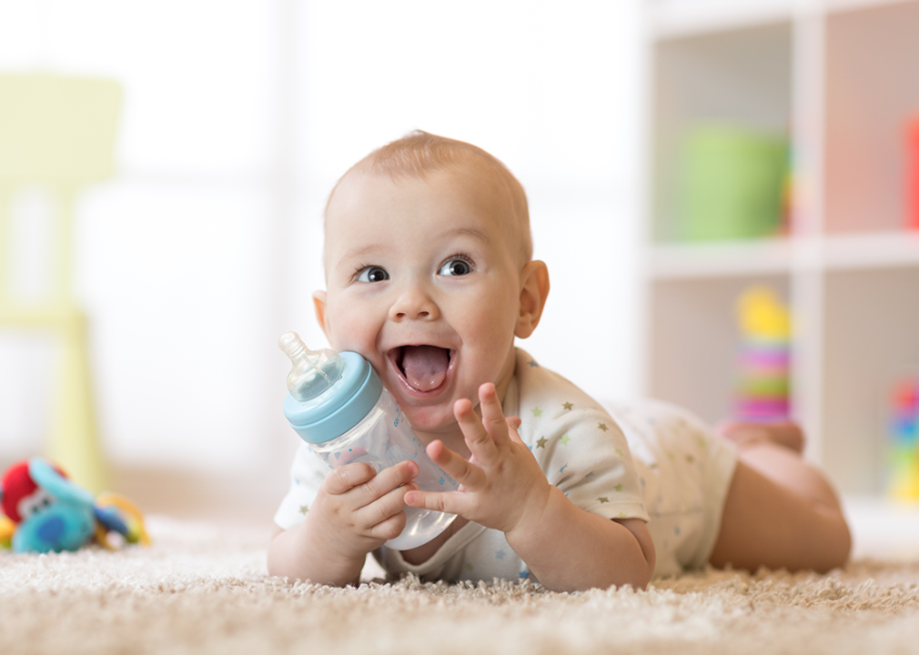 Baby holding bottle in playroom.