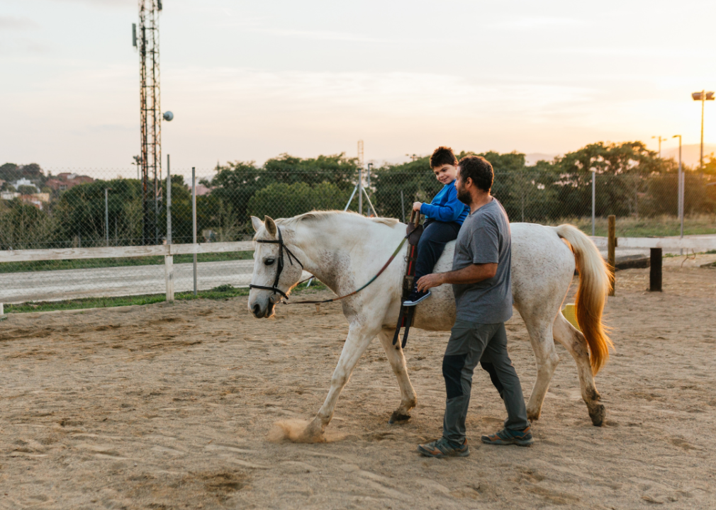 A boy with a disability riding a horse with a teacher during equine therapy.