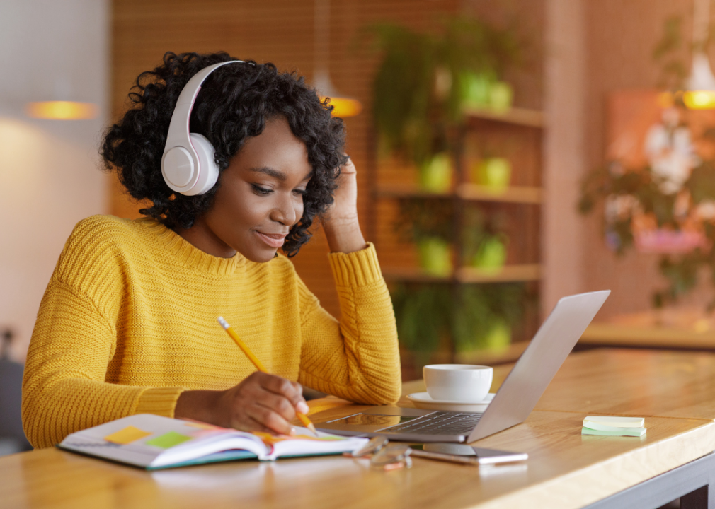 A teenager studying online wearing a headset, taking notes.