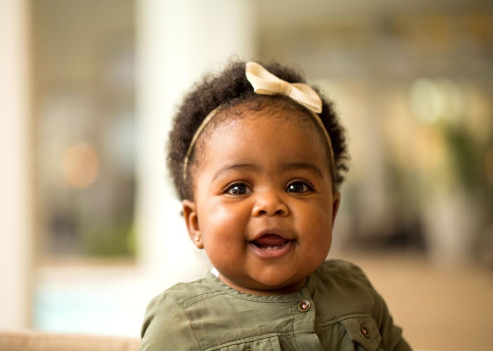 African American baby girl in green dress sitting and smiling. 