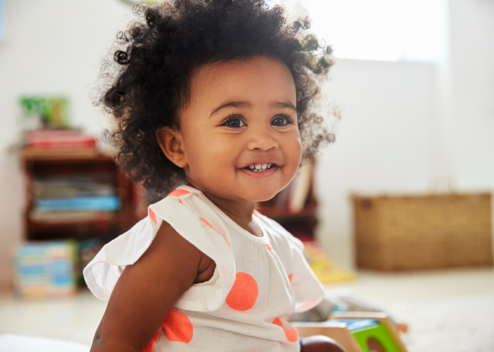 A smiley African American baby girl with curly hair smiling.