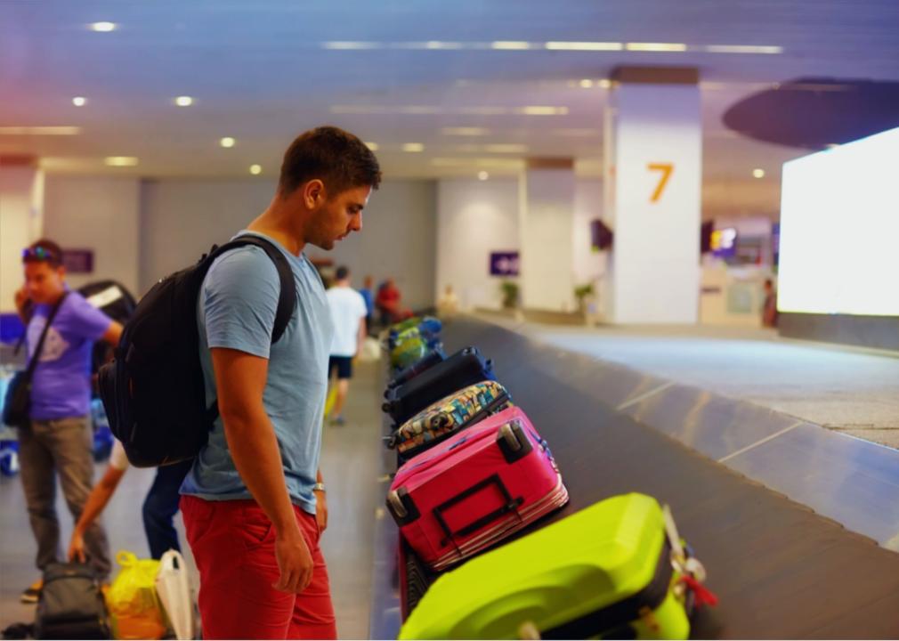 A young adult wearing a backpack looking down at the luggage carrousel with colorful bags.
