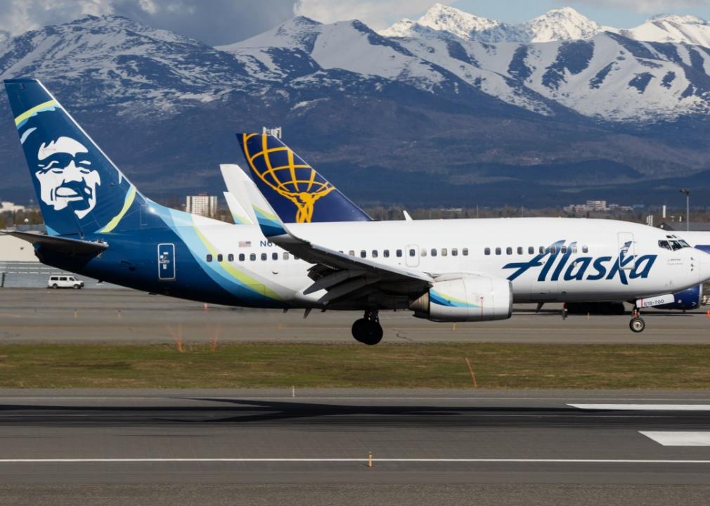 Alaska Airlines aircraft in the foreground, landing on a runway with mountains in the background.  Airline