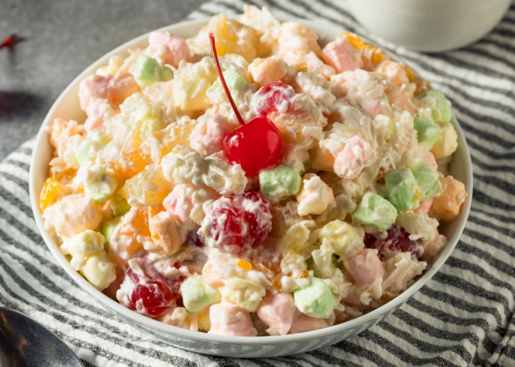 Various types of cut-up fruit in the bowl, including green grapes, red grapes, strawberries, and marshmallows with a cherry on top. 