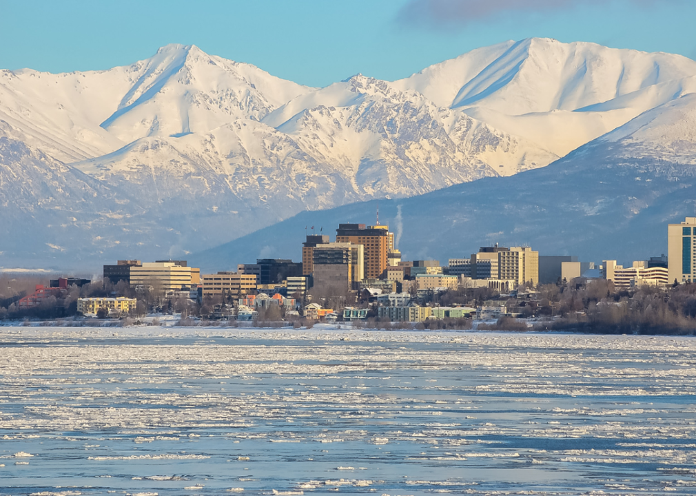 A city skyline with a frozen lake in the foreground and mountains in the background. 