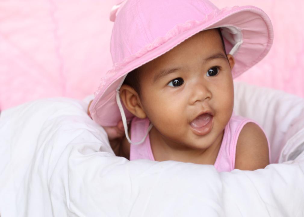 Asian baby with big black eyes wearing a pink hat and smile.