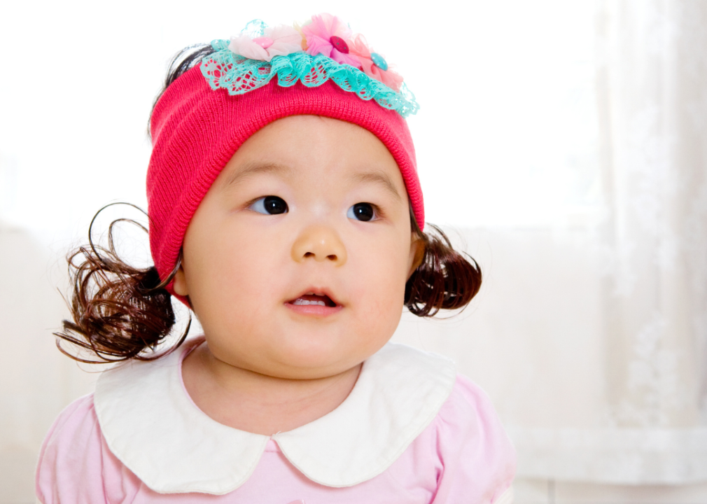 Asian baby girl with ponytails wearing a pink hat.