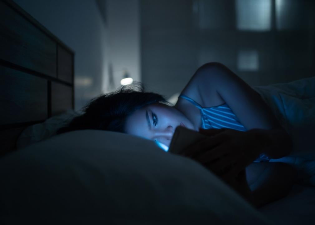 A woman looking at her smartphone in bed with blue light casting on her face.