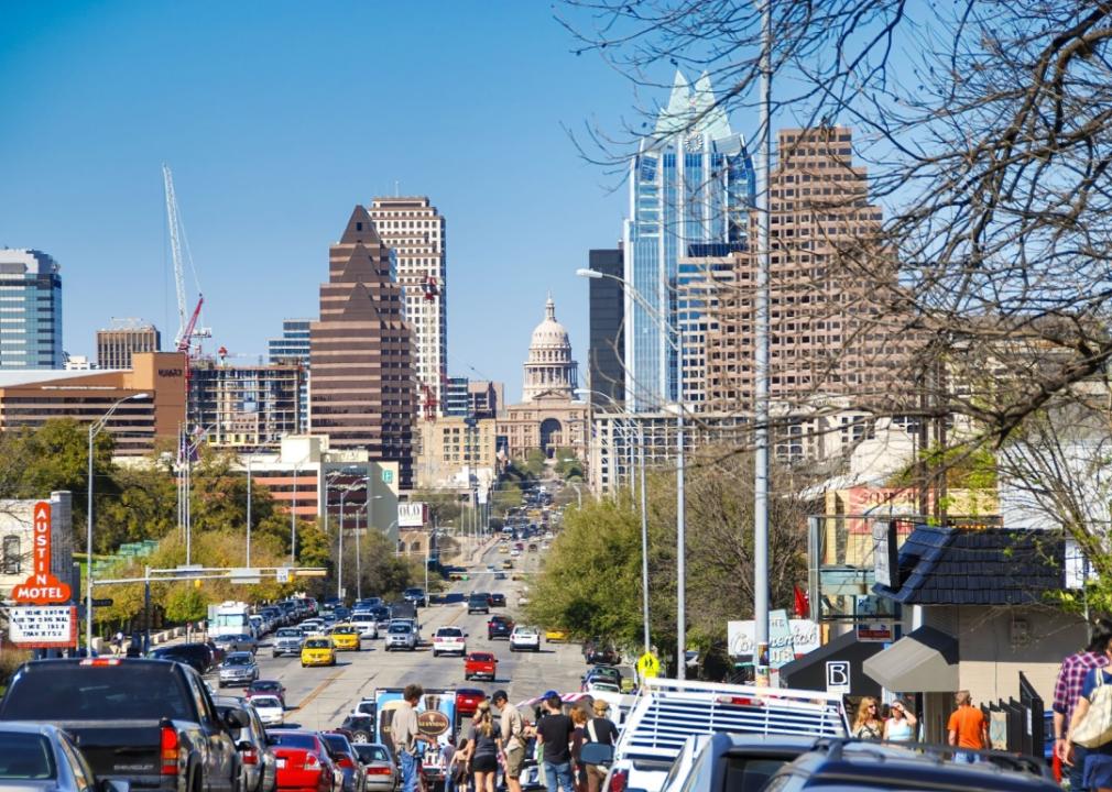 A busy city street with the building visible in the center background, with a  distinctive dome. Various modern skyscrapers and high-rise buildings in the city skyline.The street is filled with vehicular traffic, with cars densely packed and people walking along the sidewalks.