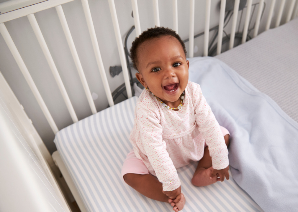 African baby girl sitting in a crib smiling.