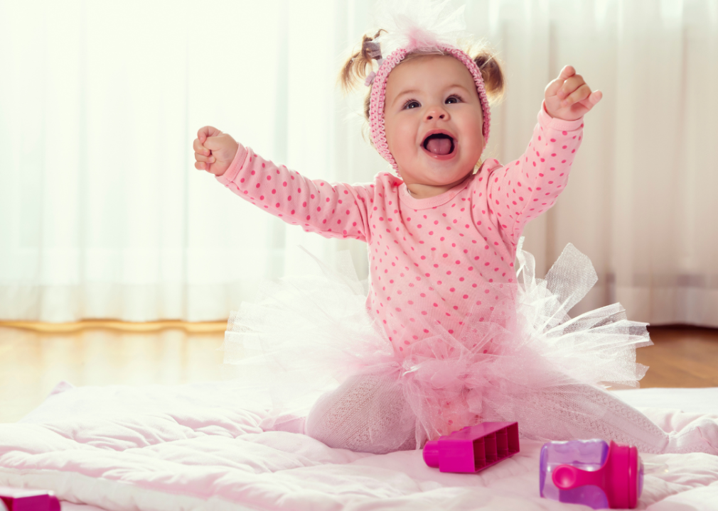 A baby girl in pink tutu dress playing and looking up.