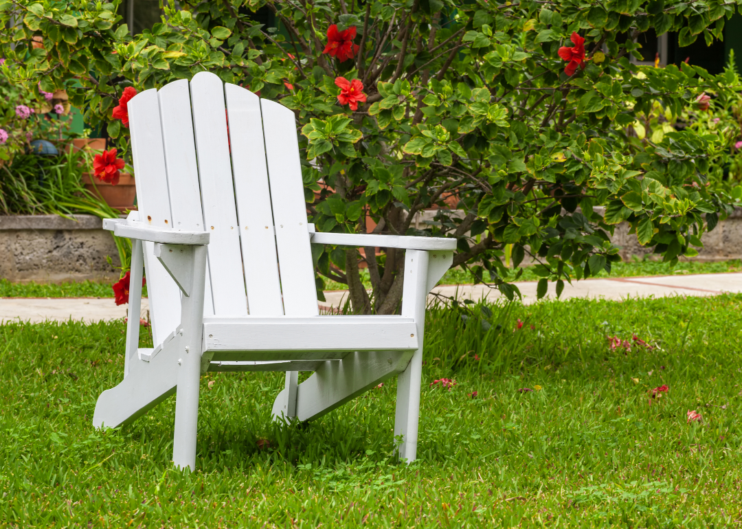 An empty white chair resting in a yard.
