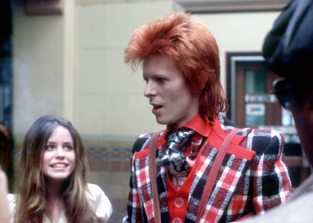 A fan smiles at Bowie, who has a bright red mullet and is wearing a red, white and blue checked suit.