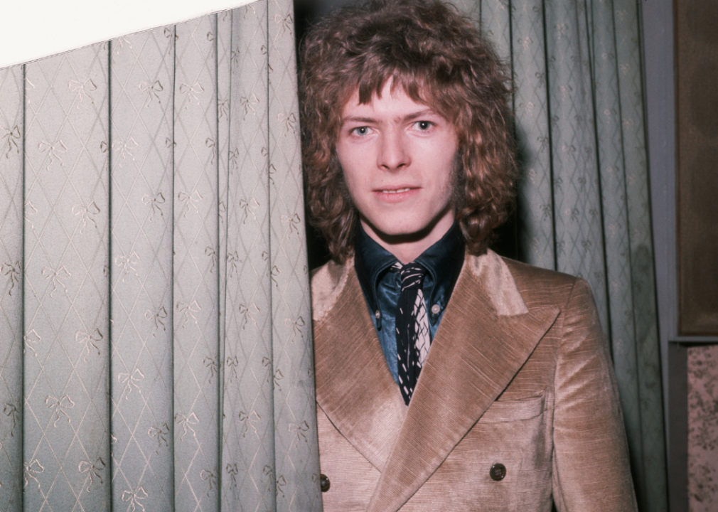 Bowie with a wavy shag haircut smiles at the camera.