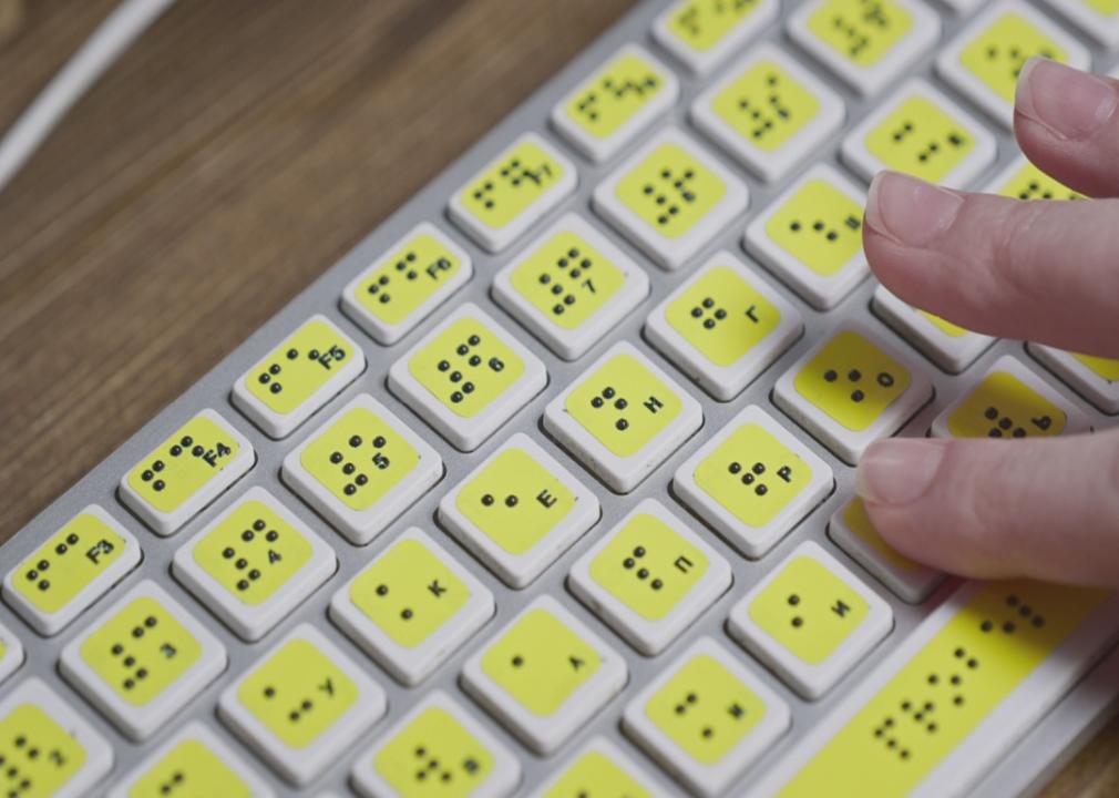 A yellow computer keyboard with braille and someone