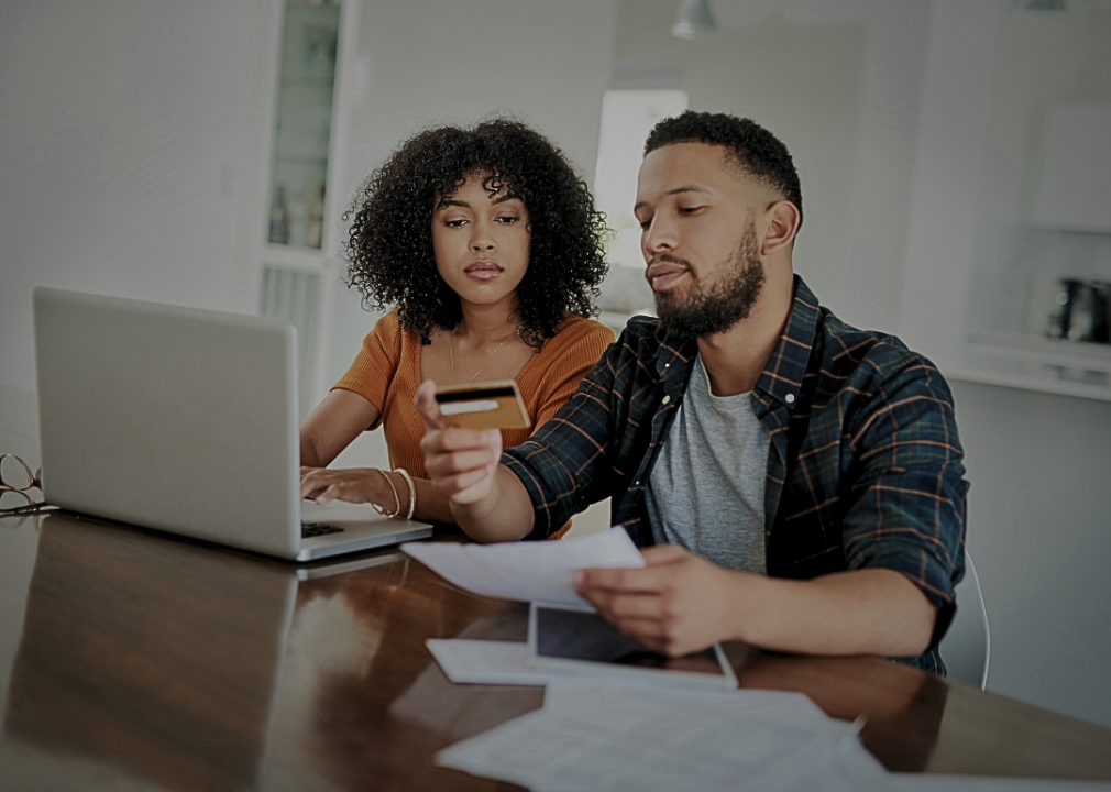 A young couple sitting at the table with a laptop, papers, and a credit card in front of them. 