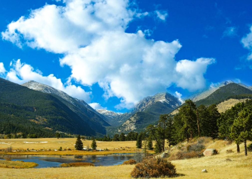 Tall, green mountains surrounding yellow grassy valley with a small lake.