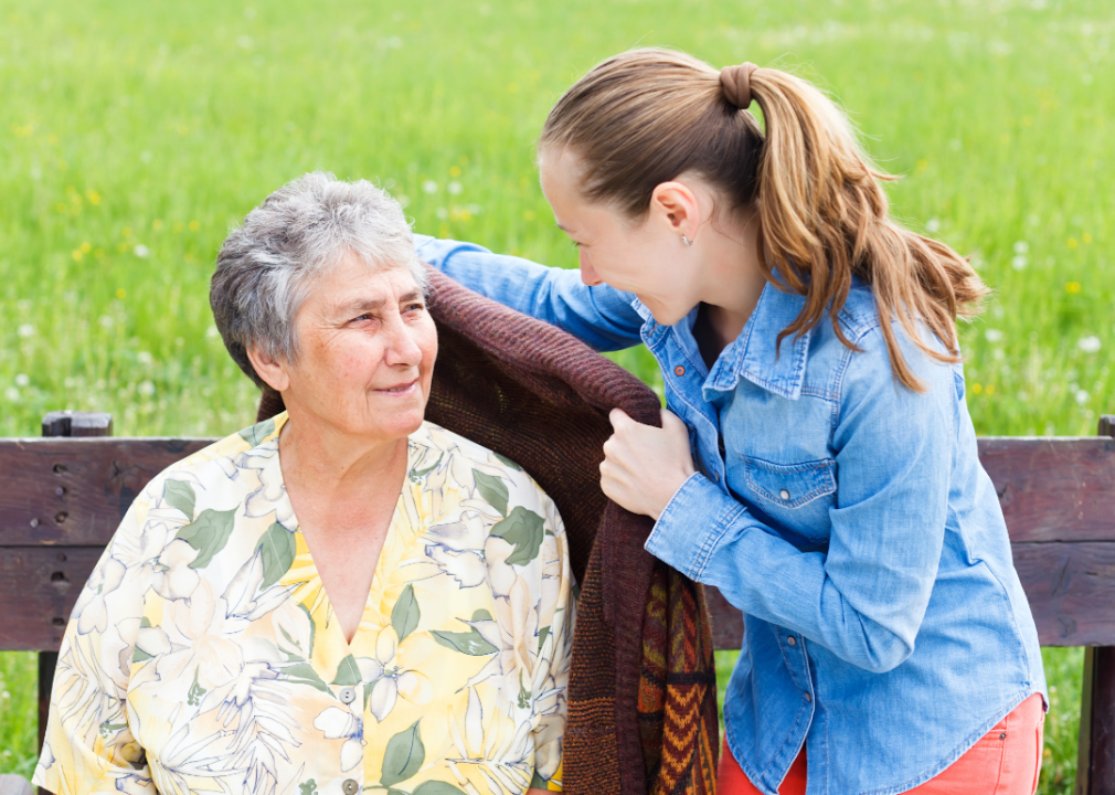 A young woman putting a jacket around an elderly woman.