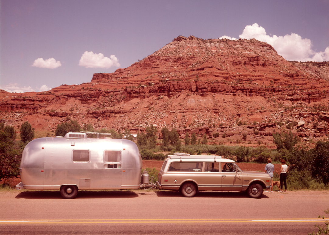 A couple looking at a mesa formation next to their station wagon.
