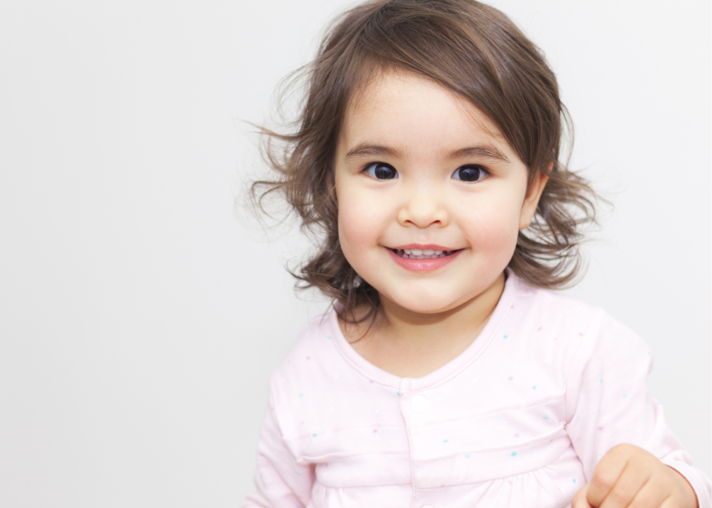 A smiling baby girl with dark brown eyes and hair.