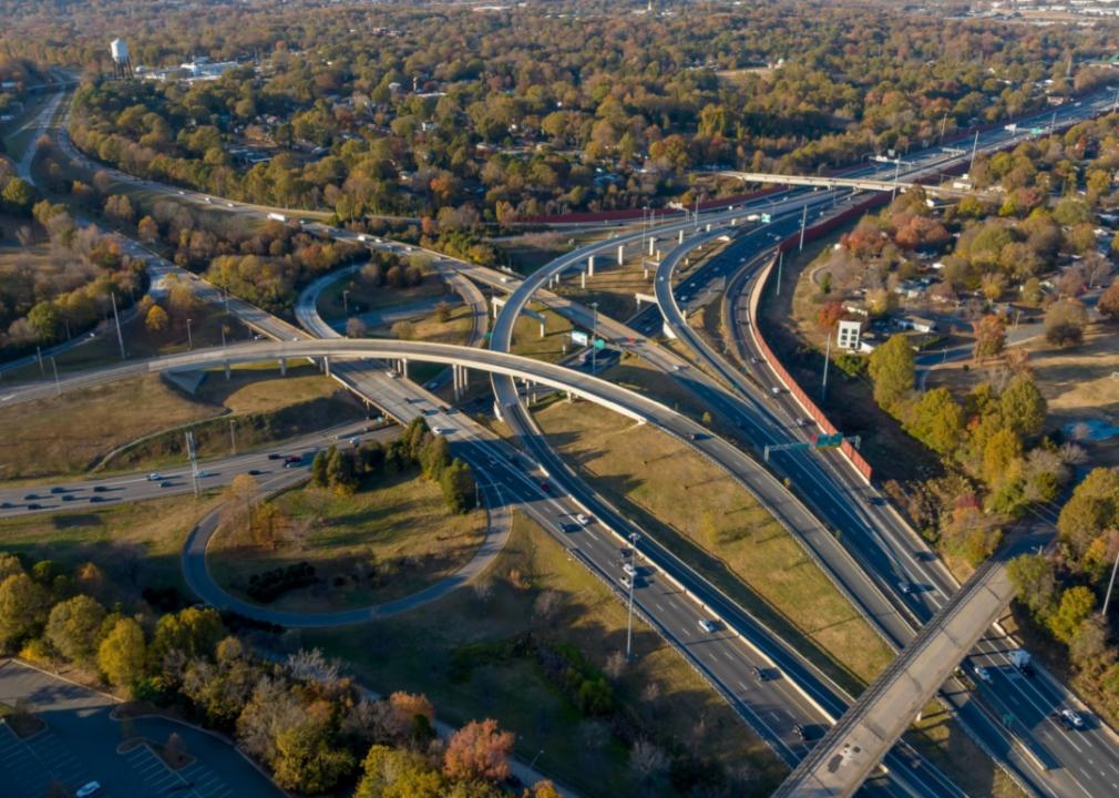 An aerial view of a complex highway interchange. Multiple levels of roads crisscross each other, with cars and trucks traveling in various directions.