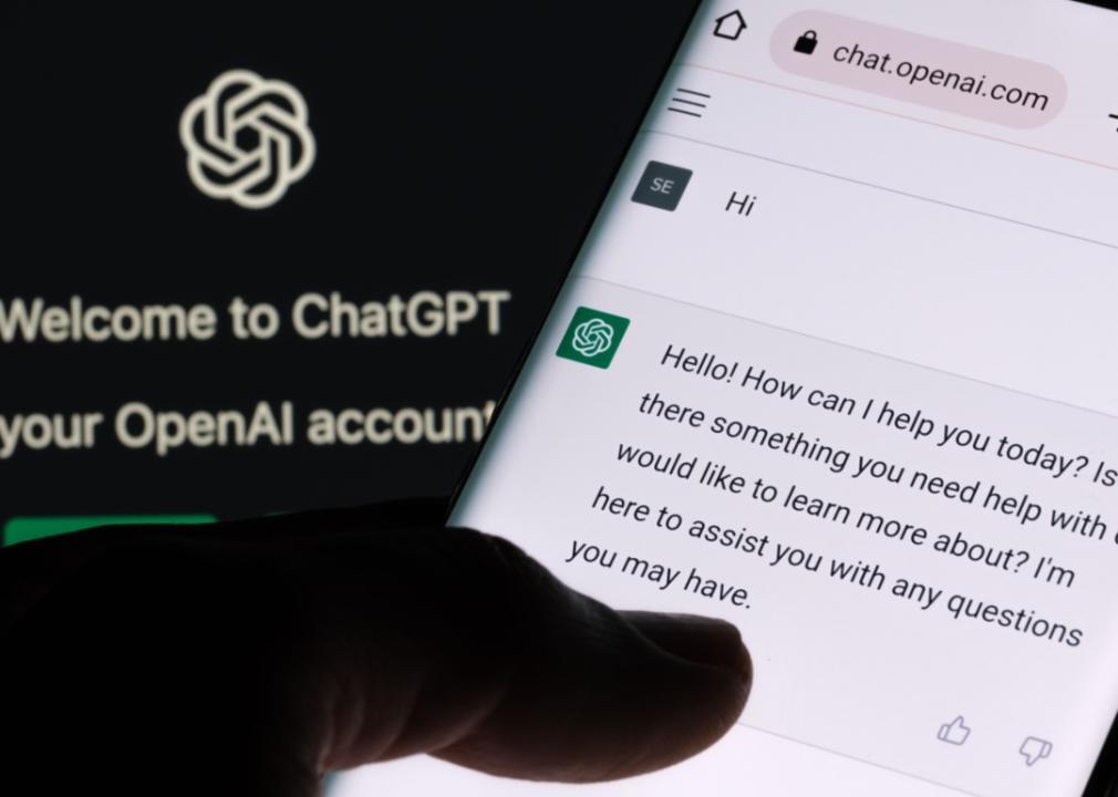 A person using ChatGPT on a smartphone. The ChatGPT logo and branding are visible on a screen in the background with the text "Welcome to ChatGPT" and "your OpenAI account." In the foreground, the smartphone screen shows an interaction with the ChatGPT interface.