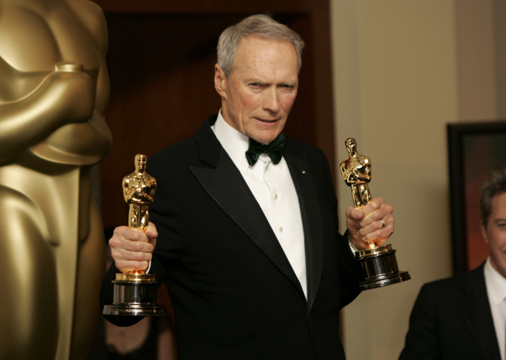 Clint Eastwood holding two Oscar statues.