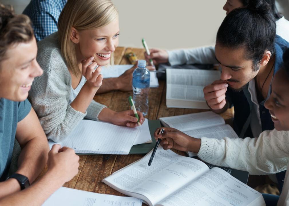 A group of students sitting around a table with open books, notebooks, and pens.