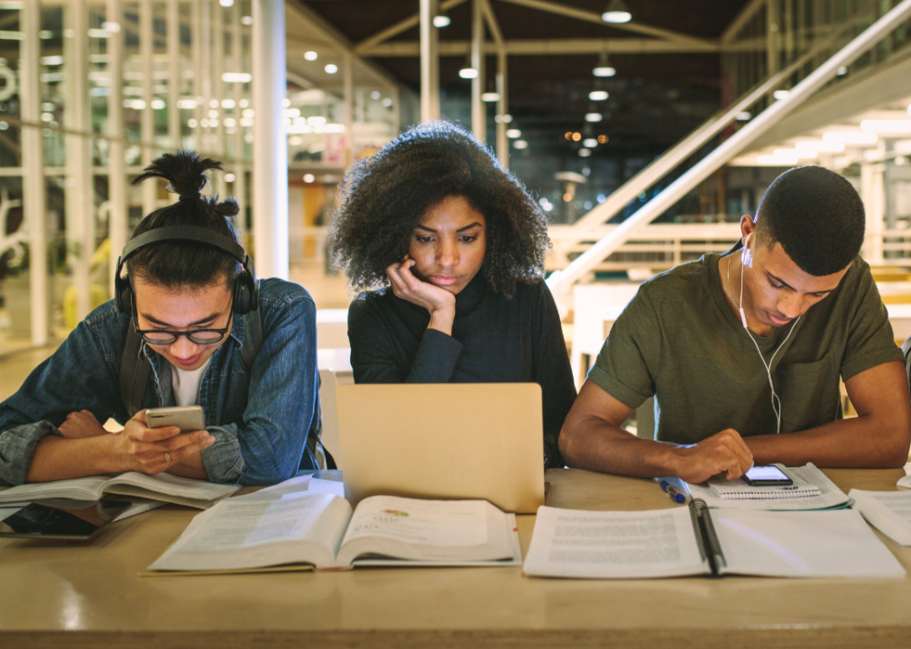 Three college students fixated on their laptops and smartphones.